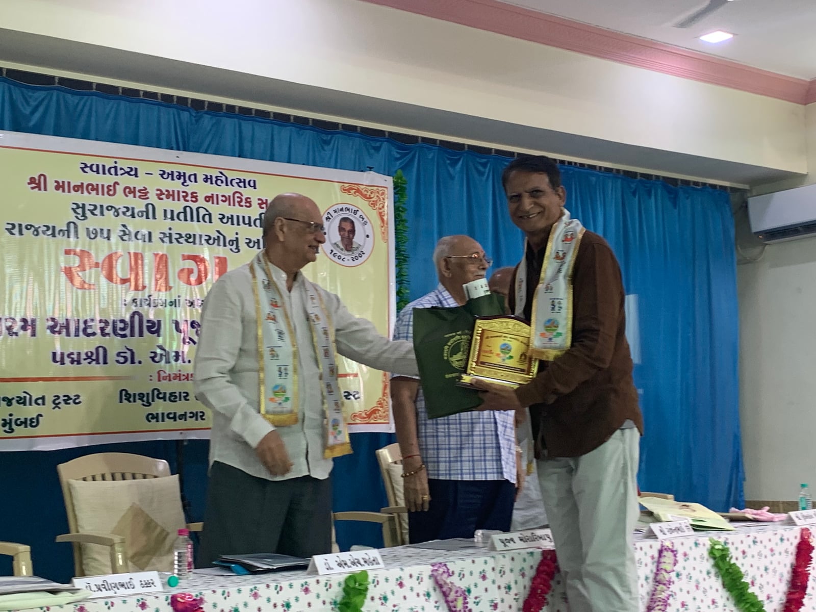 The award being presented on stage at the ceremony in Bhavnagar, under a banner welcoming 75 service organisations of the state