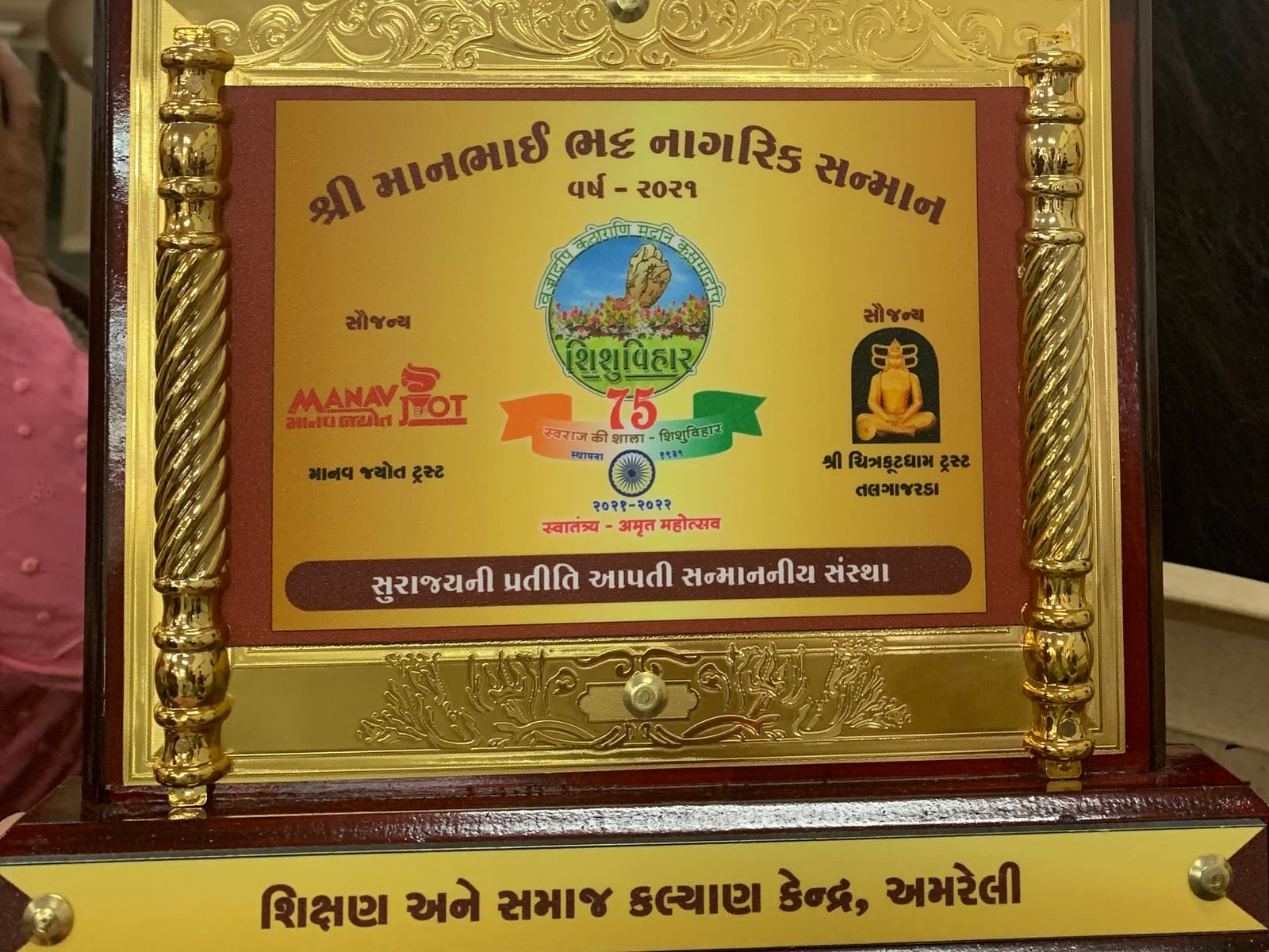 The Maanbhai Bhatt Nagrik Sanman plaque, engraved “વર્ષ ૨૦૨૧” and, along the base, “શિક્ષણ અને સમાજ કલ્યાણ કેન્દ્ર, અમરેલી”