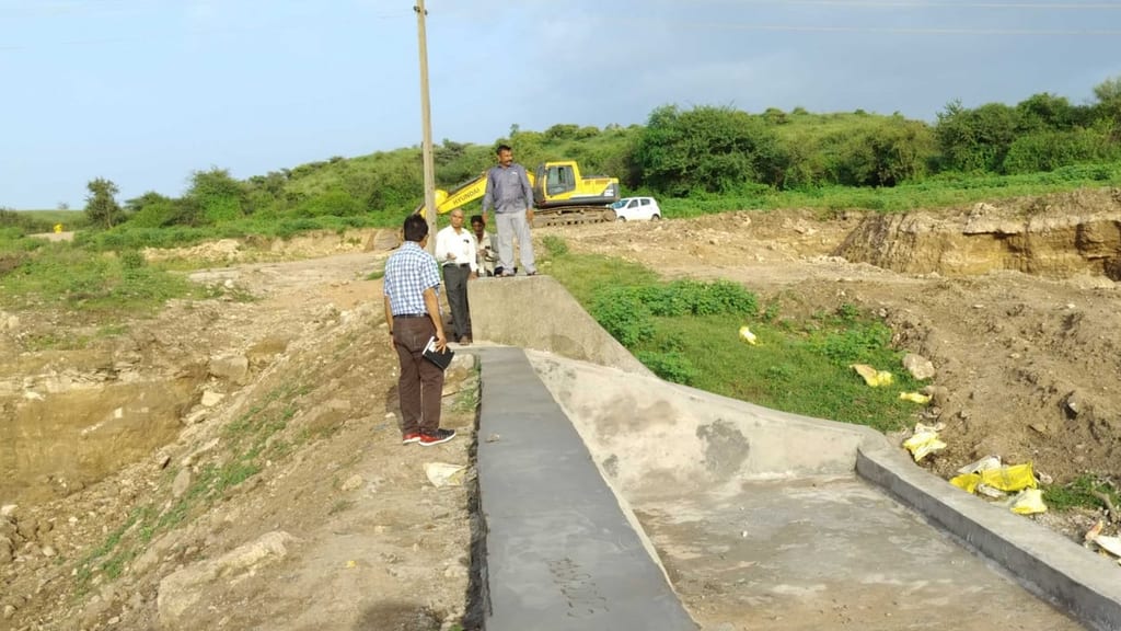 Men standing on the newly concreted spillway of the Mota Umarda check dam, with an excavator still working on the desilted bed behind them