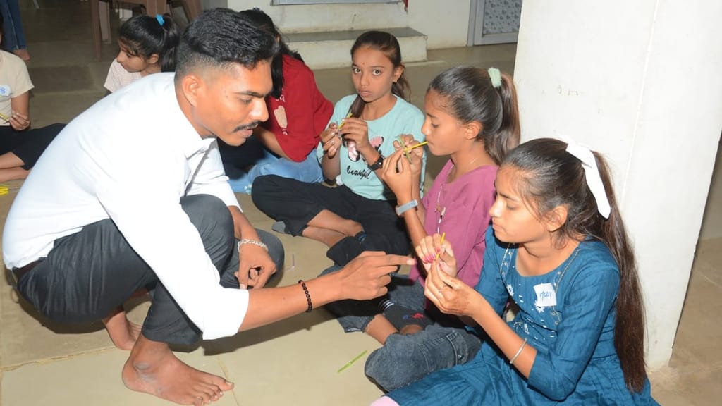 A facilitator crouching on the floor with a group of girls, each holding a cut drinking straw to her lips