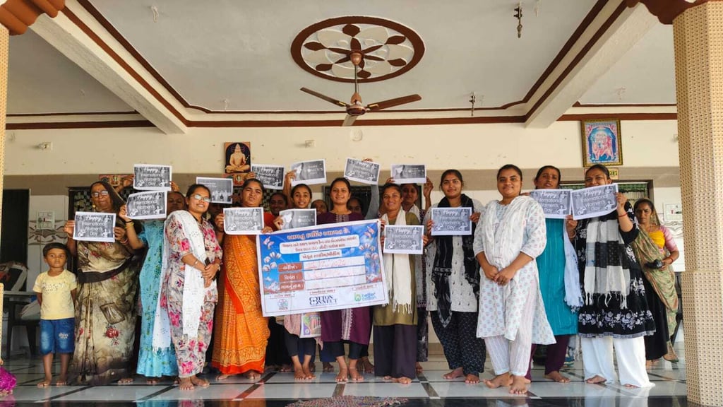 Women standing together in a village hall at Sanosari, each holding up a printed “Happy International Women’s Day” sheet